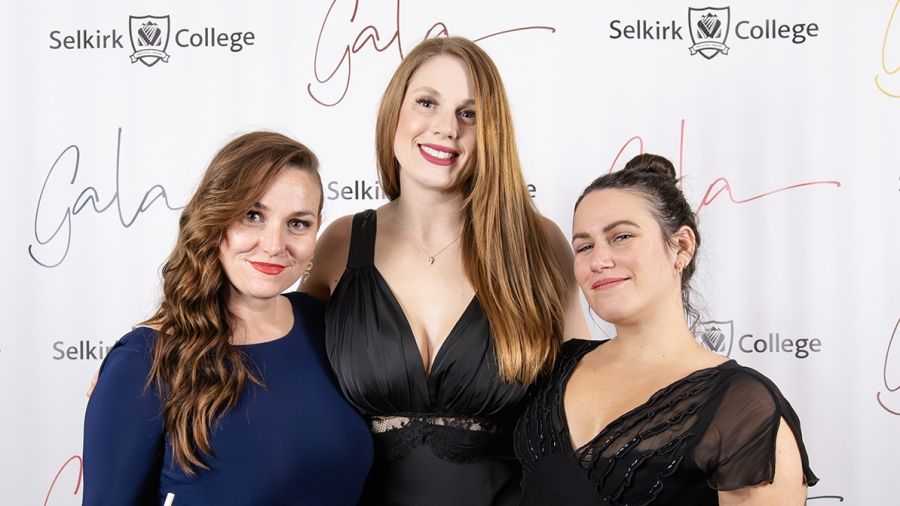 Three women smile in front of a banner that reads Selkirk College Gala