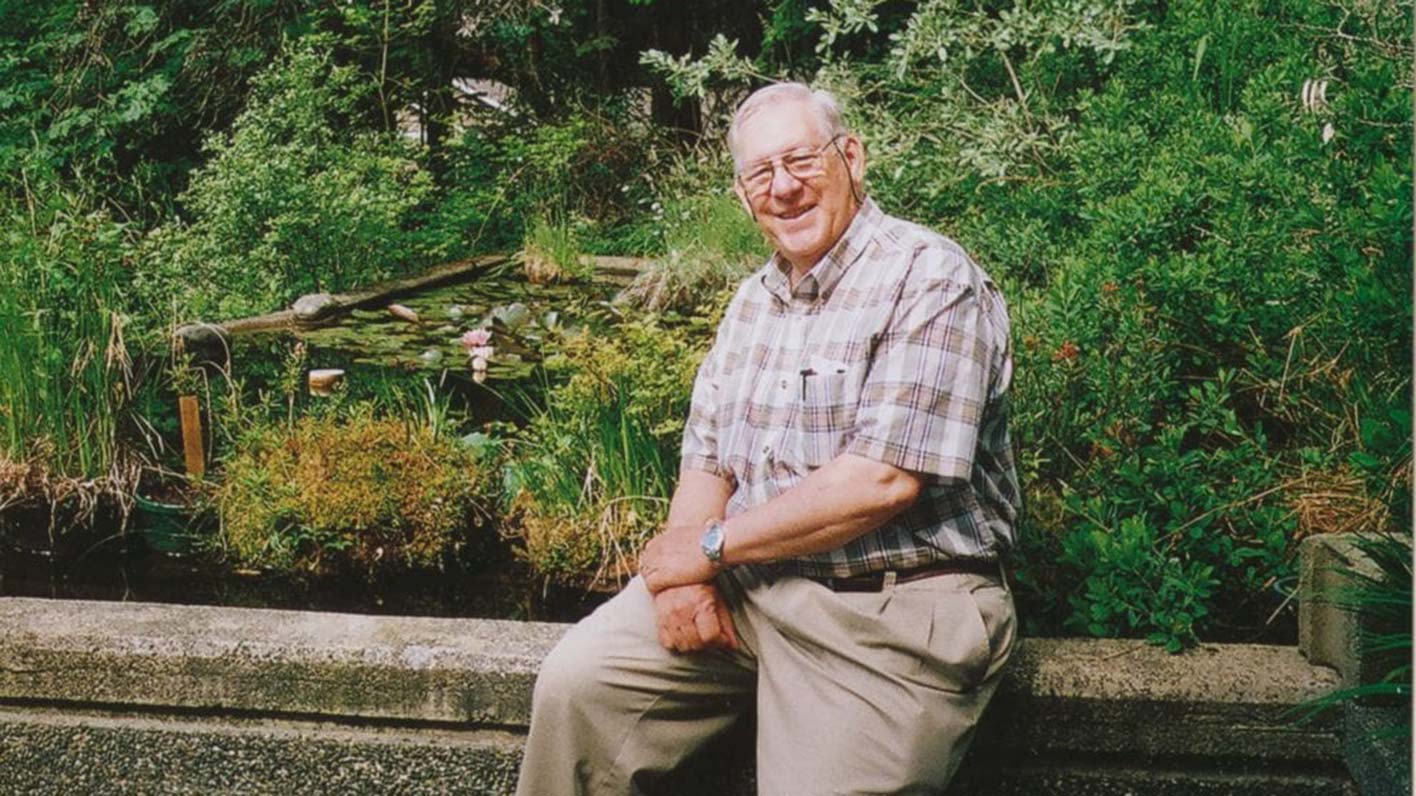 Bill Merilees sits outside in a garden smiling