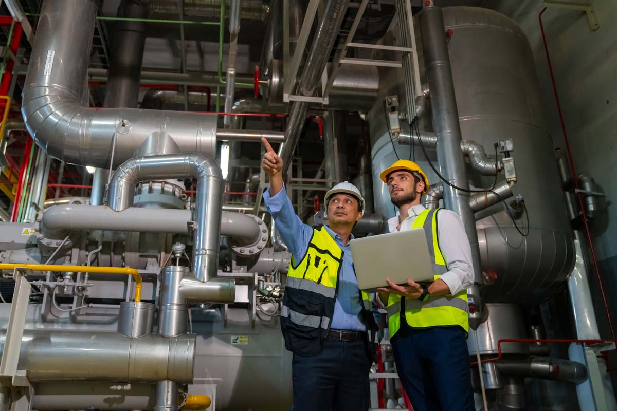 Two workers wearing yellow vests stand in a factory