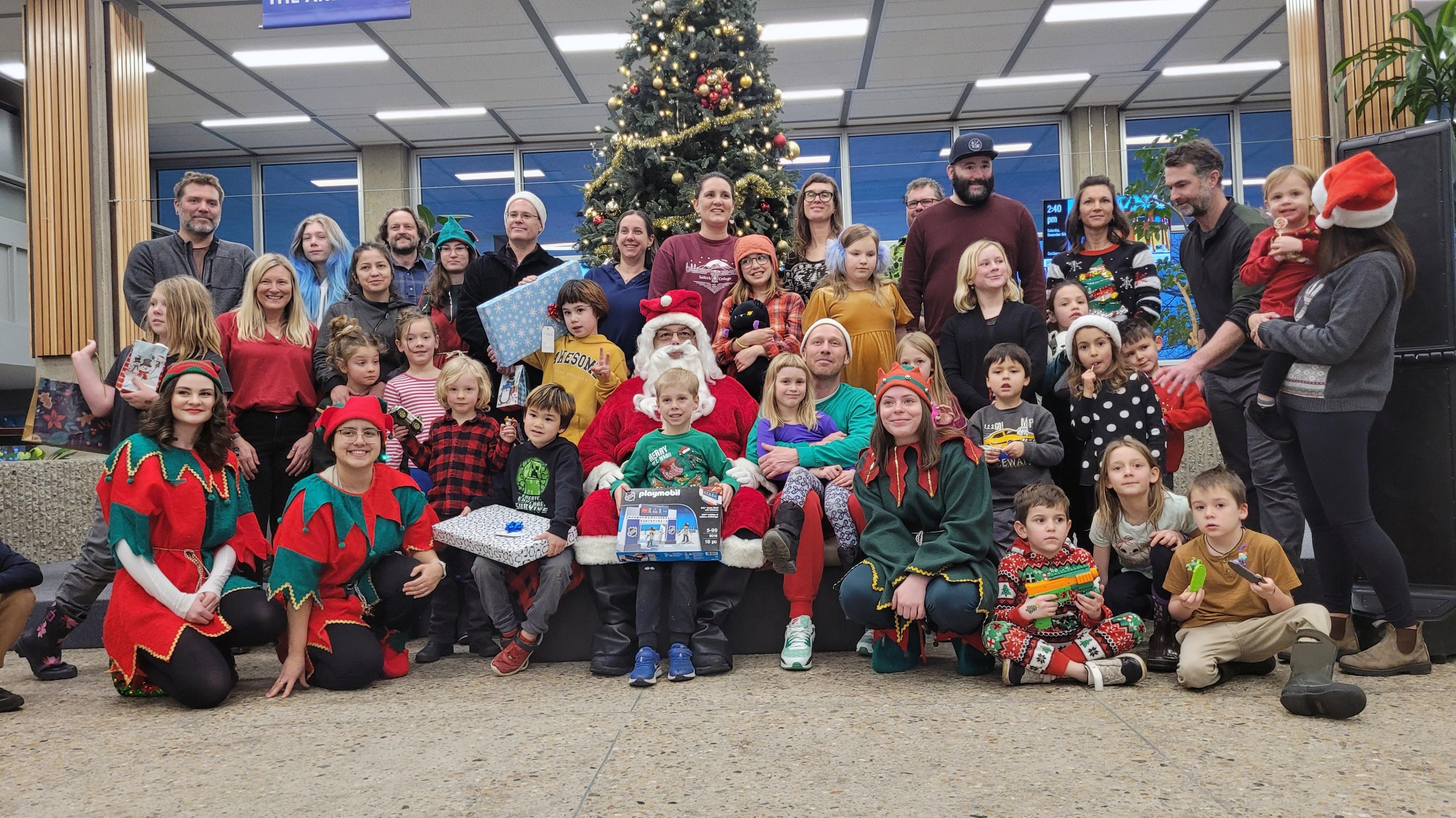 A group of employees and their children sit around Santa Claus in front a large Christmas tree