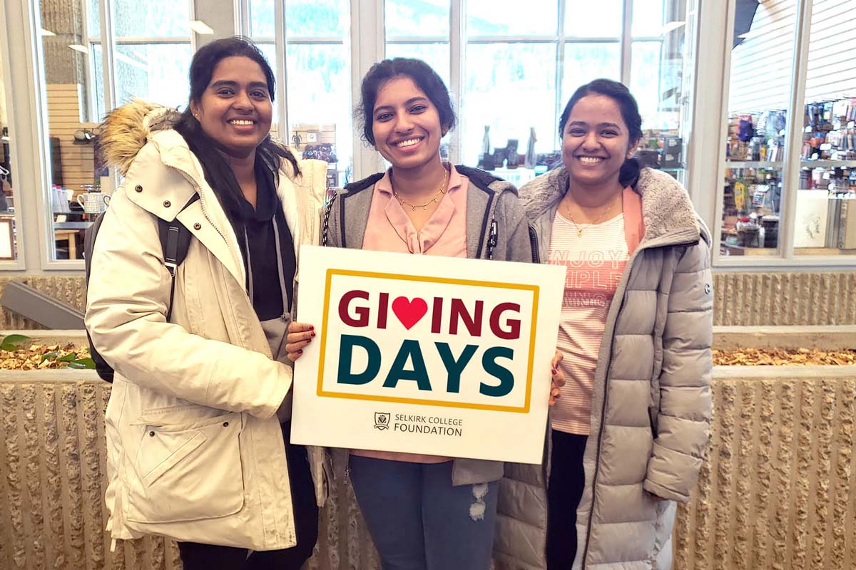 Three students stand holding a sign that reads &quot;Giving Days&quot;