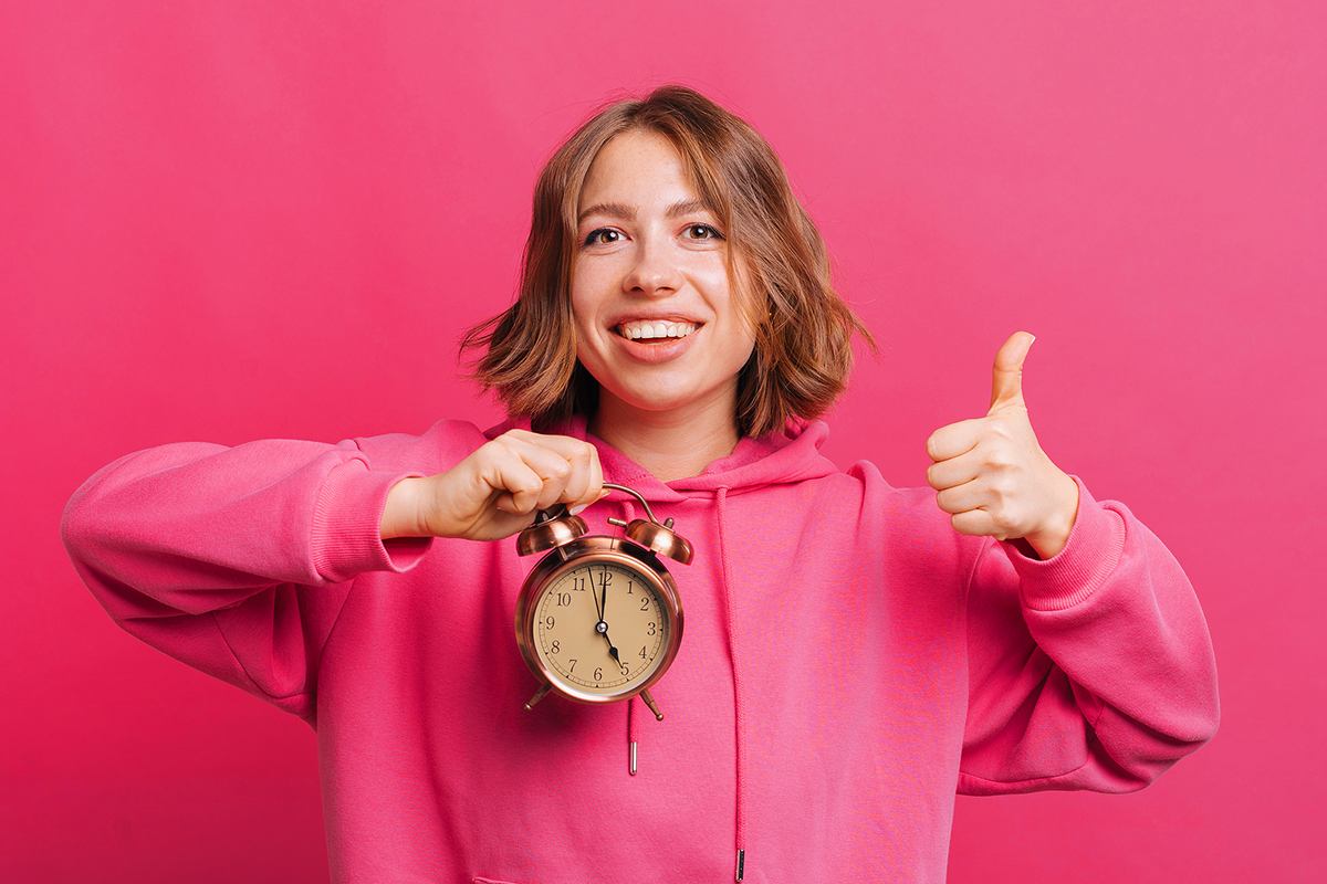 Lady holding up an alarm clock smiling