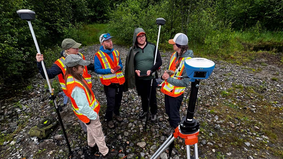 A group of interns wearing high-visibility vests stand in a circle with equipment