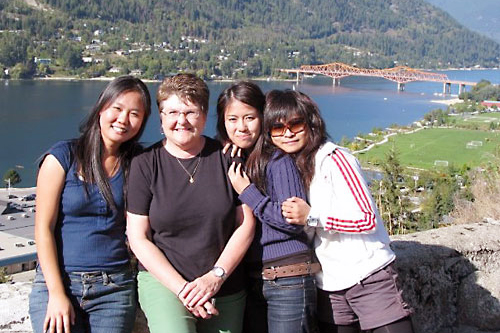 A group of people smile against the backdrop of Kootenay Lake and the Big Orange Bridge