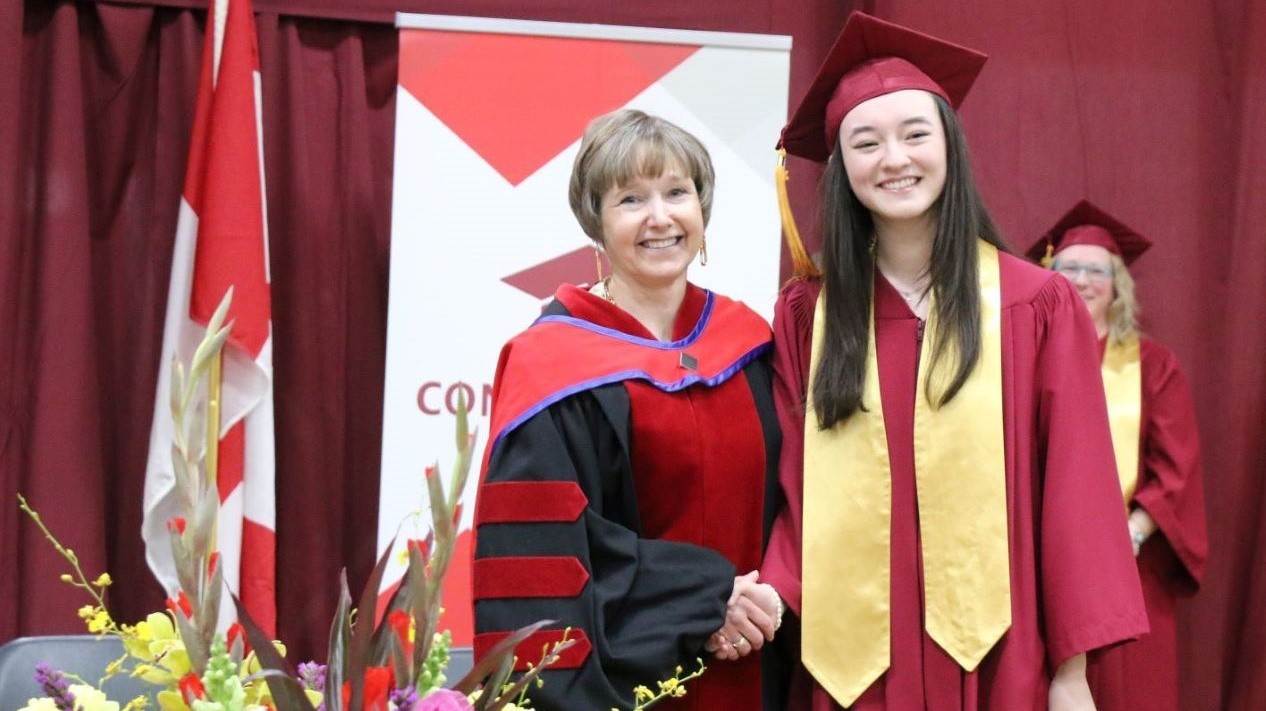 President Maggie Matear shakes hands with a student at Convocation
