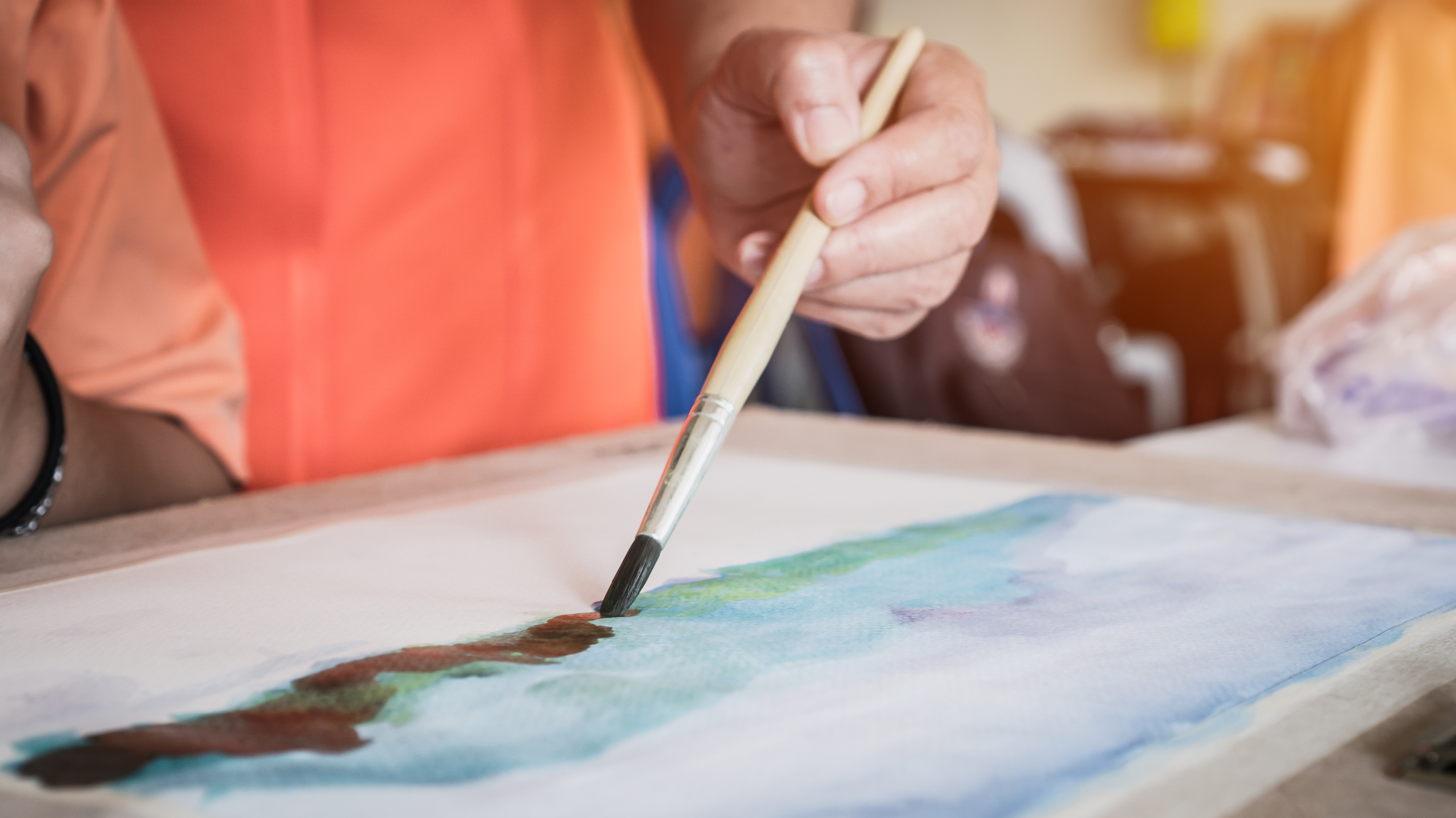 A hand holding a brush painting a watercolour painting