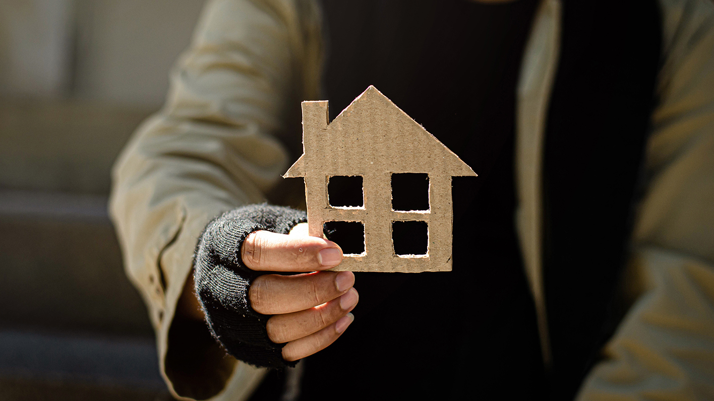 homeless man holding up a cardboard house
