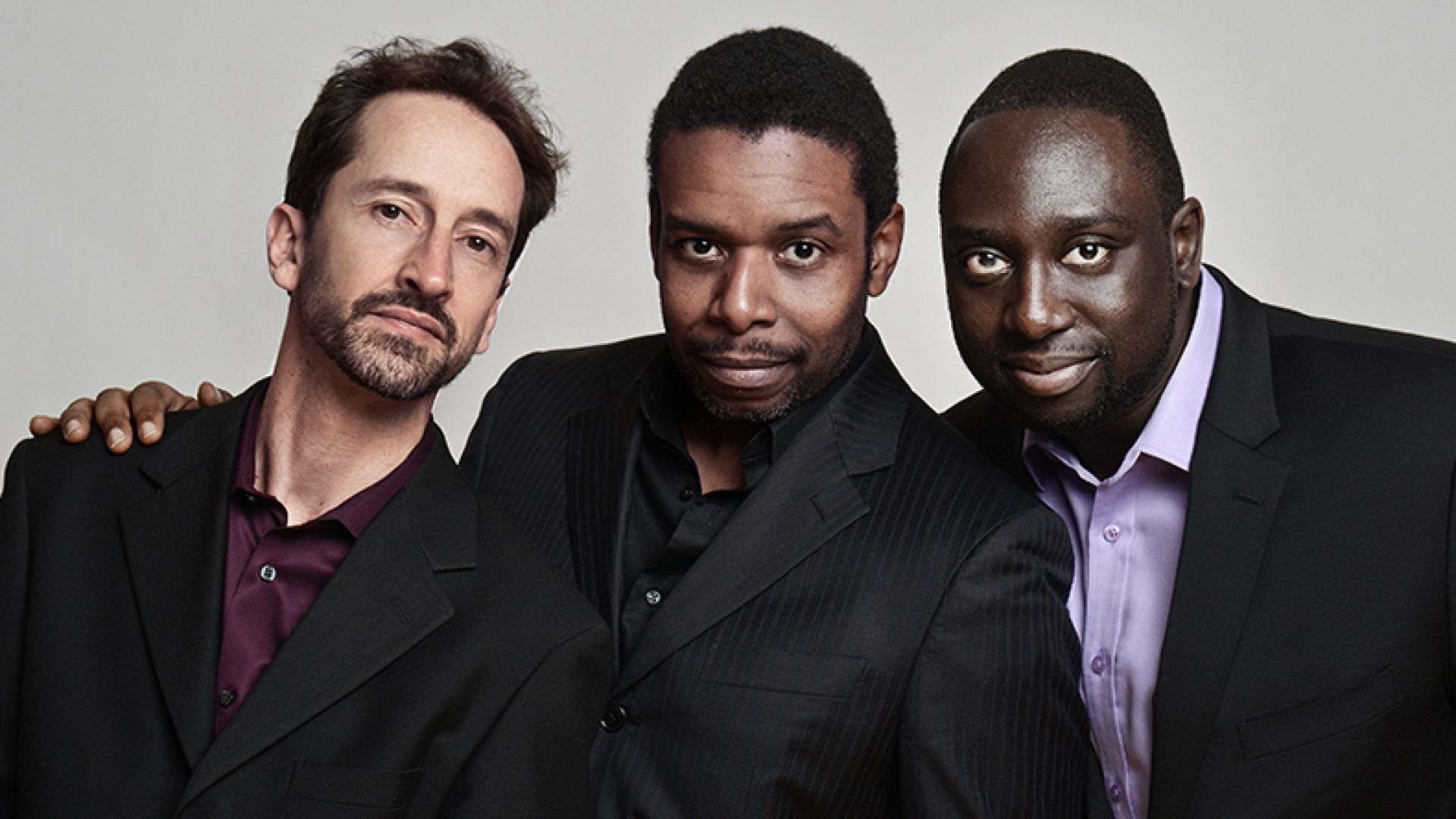 Three male musicians in black suits stand together
