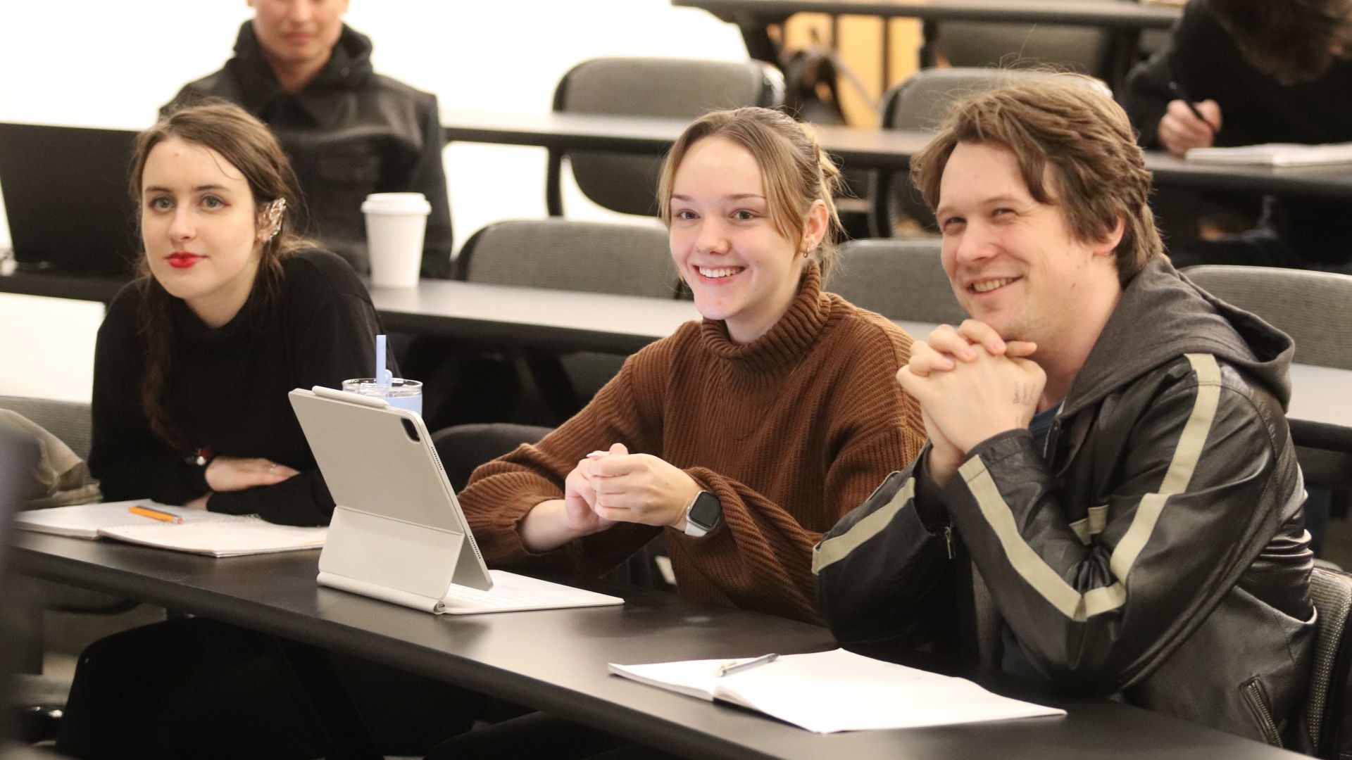Three smiling students sit in a classroom.