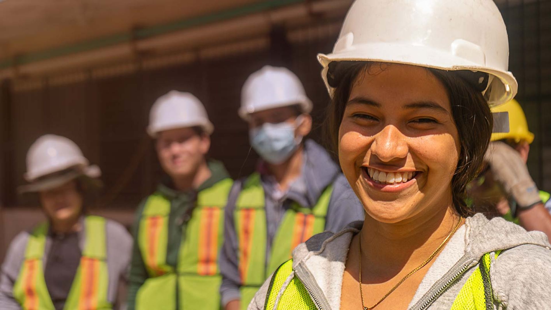 Workers wearing hard hats and vests stand in a row