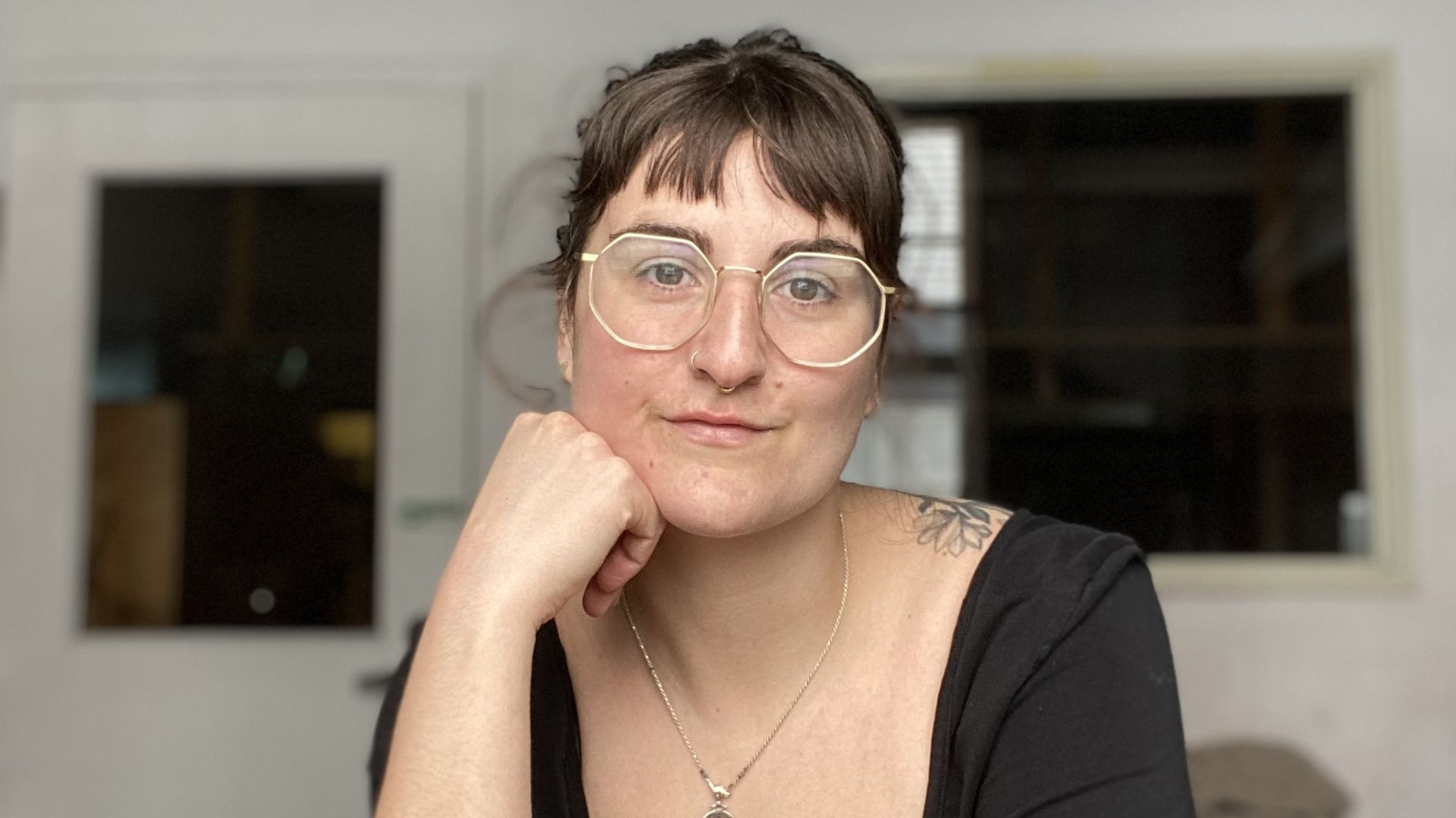 A woman sits leaning on her hand looking into the camera