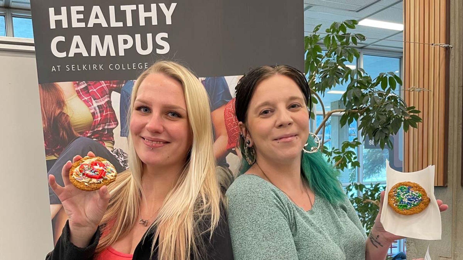 Two students stand holding cookies and smiling