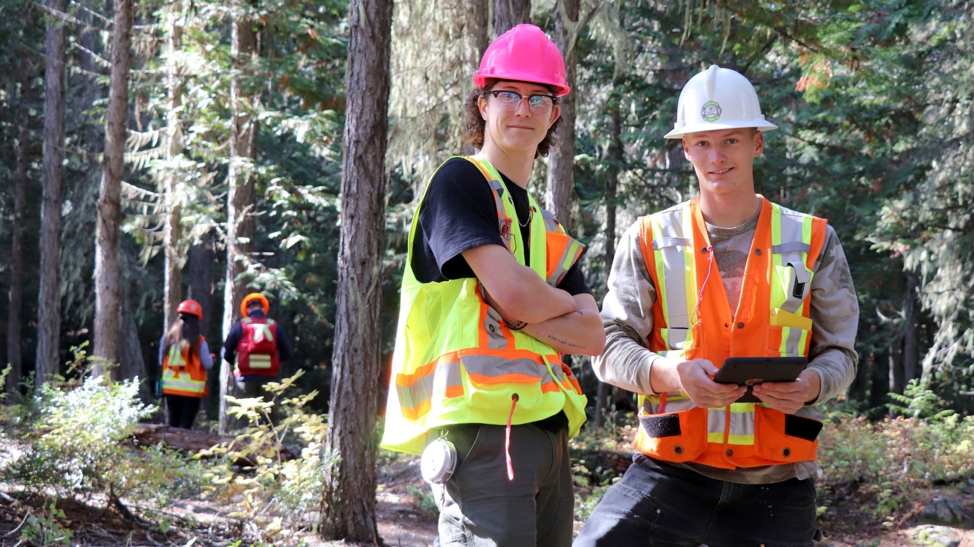 Two male students stand in high-vis vests in the forest