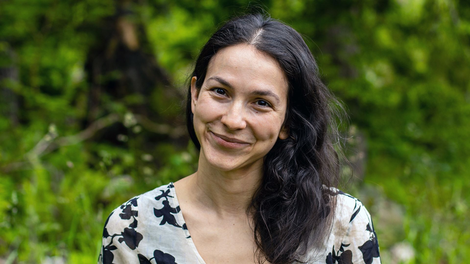 Sharon Stein smiles against a backdrop of green foliage