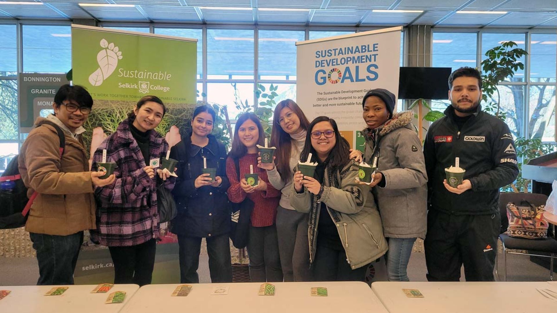 A group of students stand holding potted plants