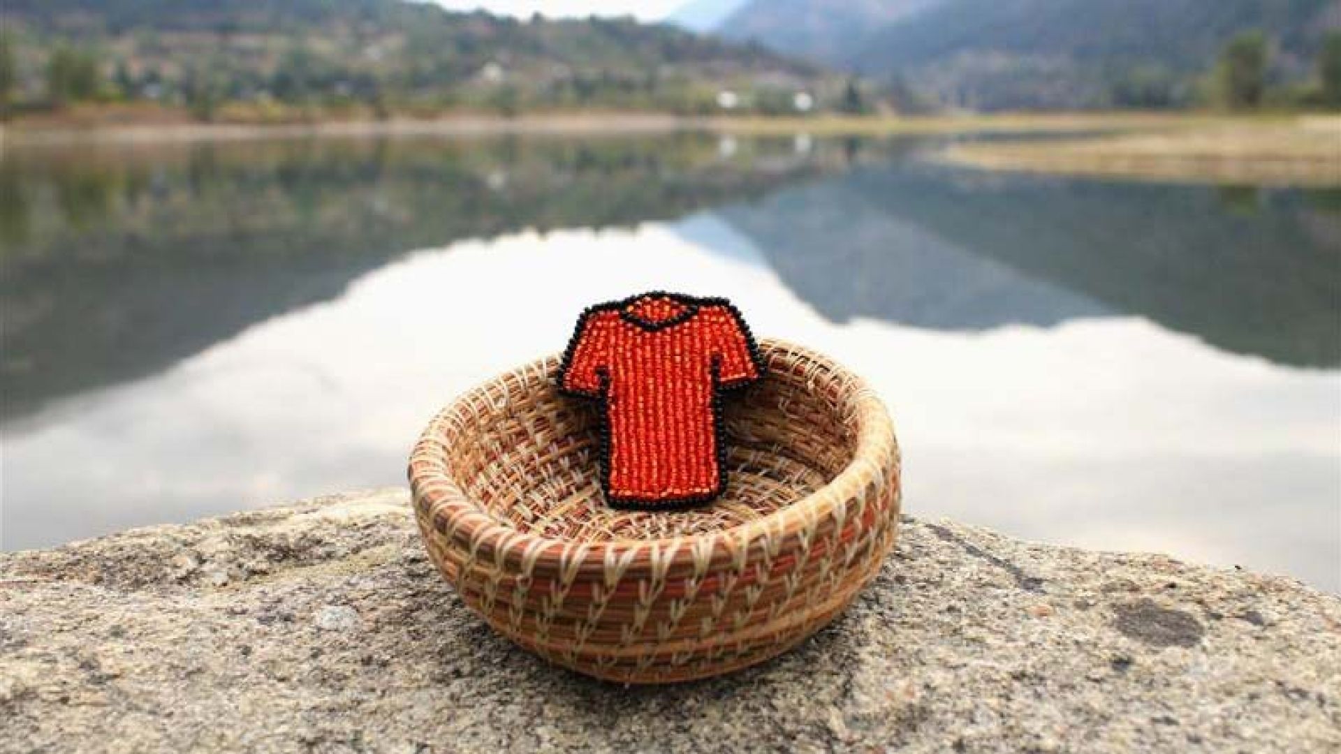 A beaded orange shirt in a basked next to a lake