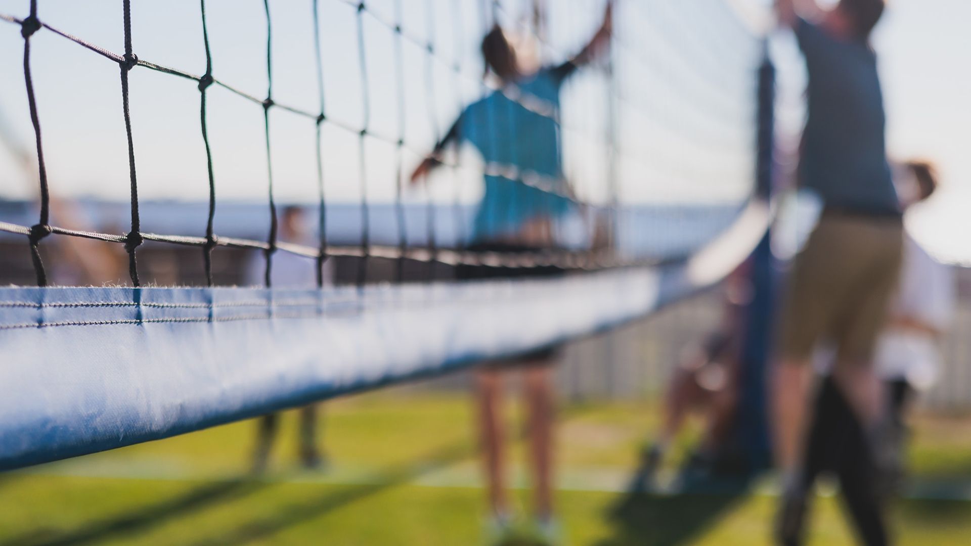 A close-up of a volleyball net with players spiking the ball