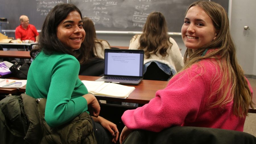 Two students sit in class smiling in front of a laptop