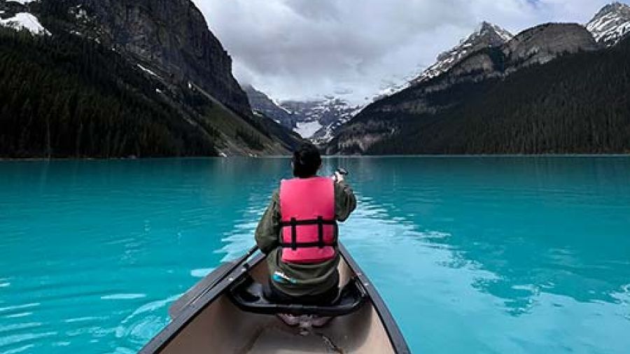 A person sits in a canoe on a lake surrounded by mountain peaks