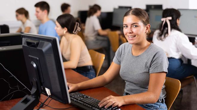 A student sits at a computer smiling