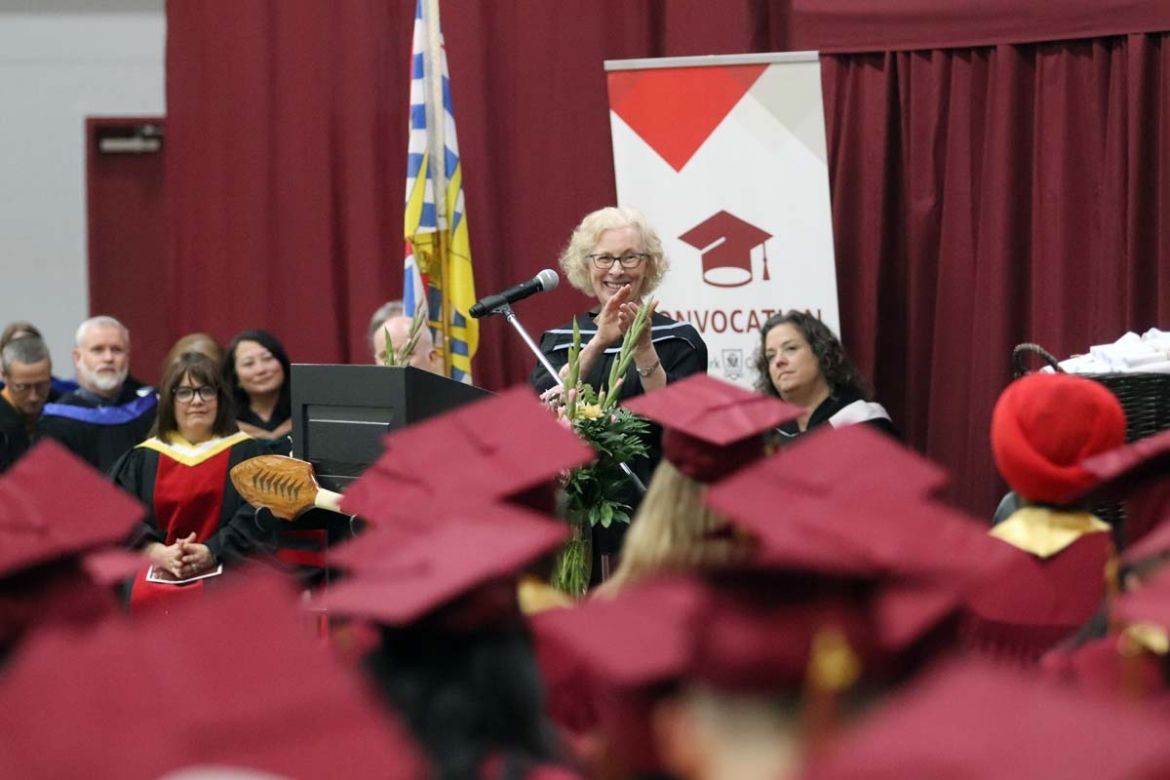 The chair of the board of governors stands at a podium during convocation smiling