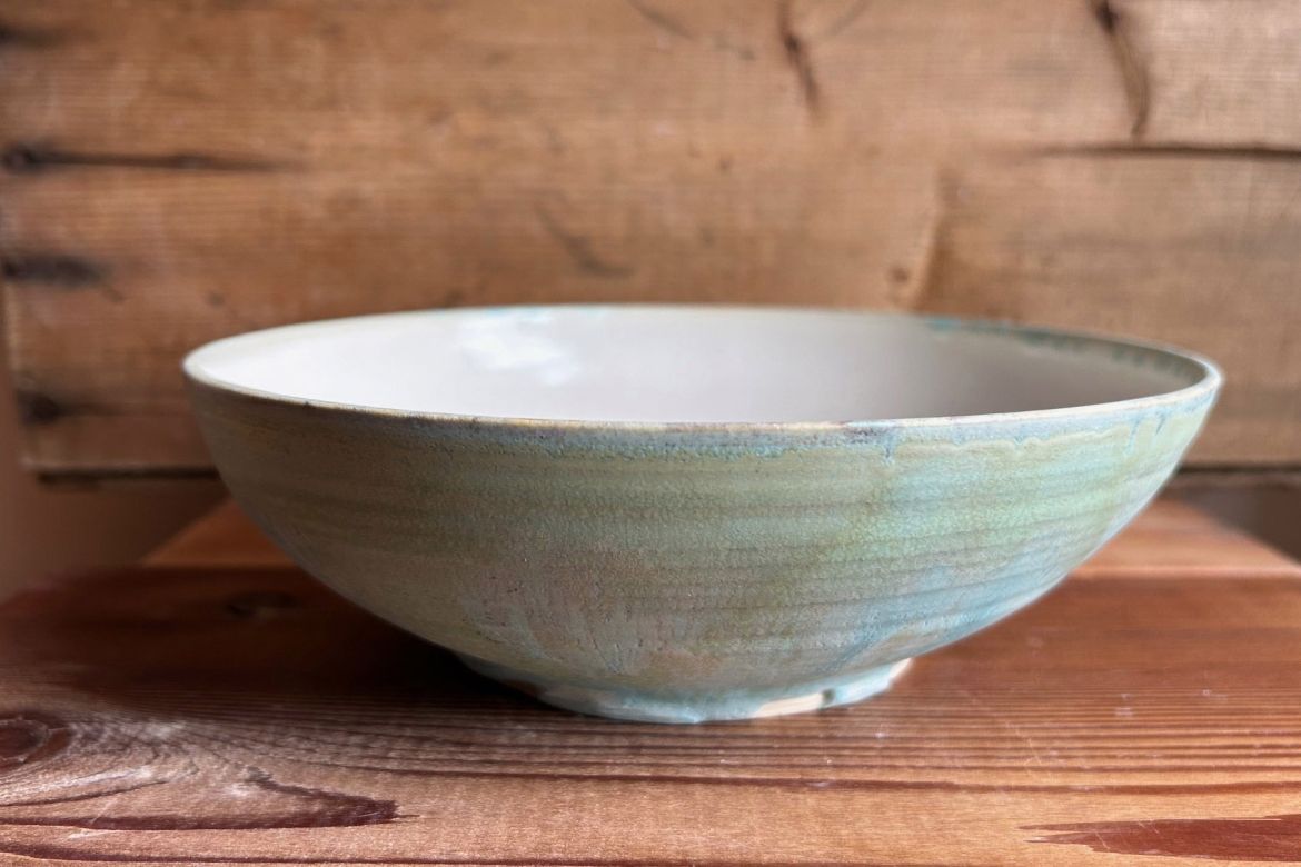 A green handmade ceramic bowl sitting on a wooden table