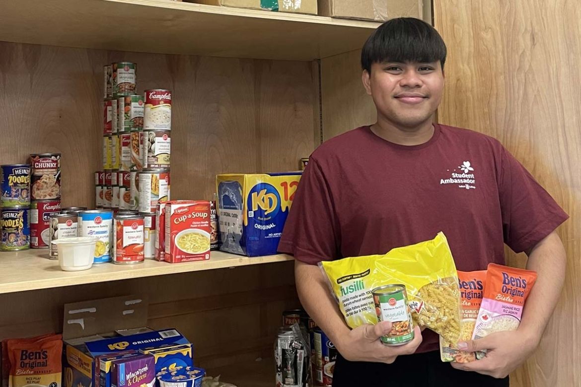 A student stands in the Food Pantry holding non-perishible food items