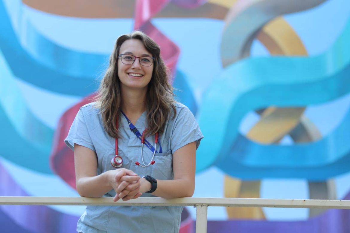 A student in scrubs stands in front of a mural
