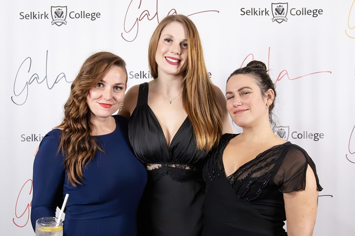 Three women smile in front of a banner that reads Selkirk College Gala