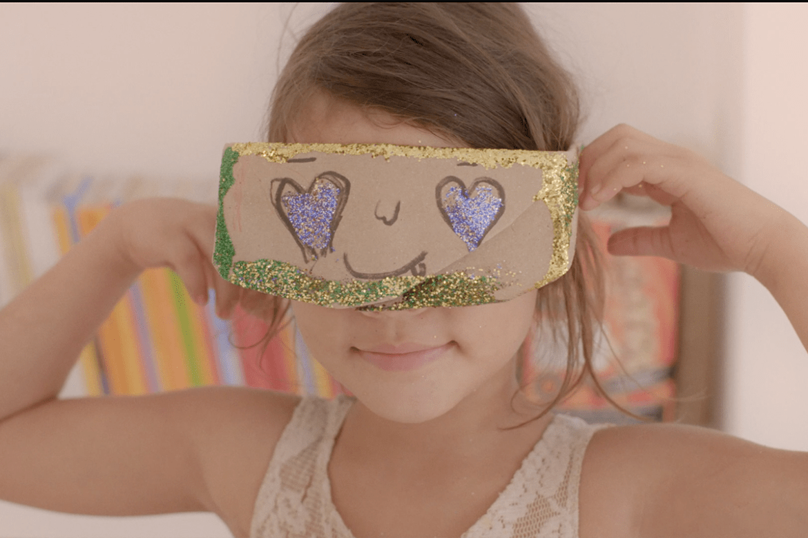 A girl holds up a cardboard mask