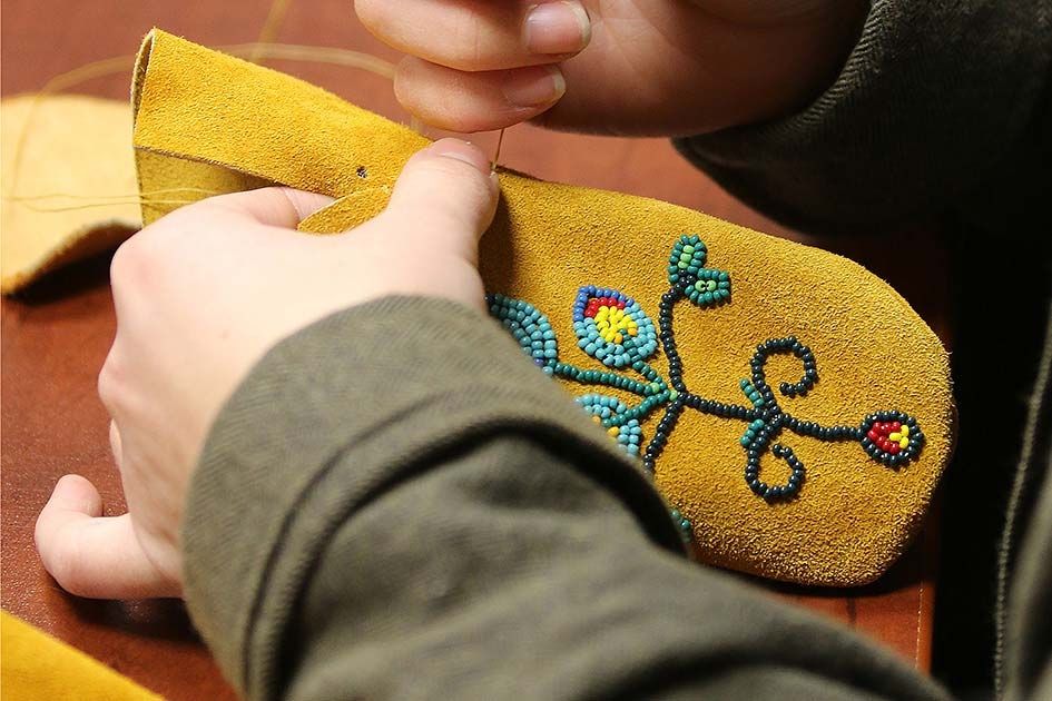 A person sews beads onto a pair of moccasins