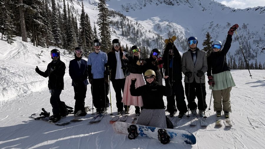 Skiers and snowboarders stand on the mountain in black-tie attire