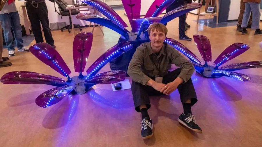 A student sits in front of a flower sculpture made of steel, purple acrylic and polycarbonate