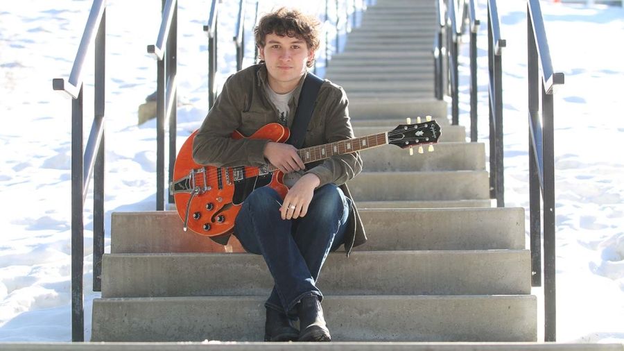 Music student Aaron Pasecreta with his guitar on stairs