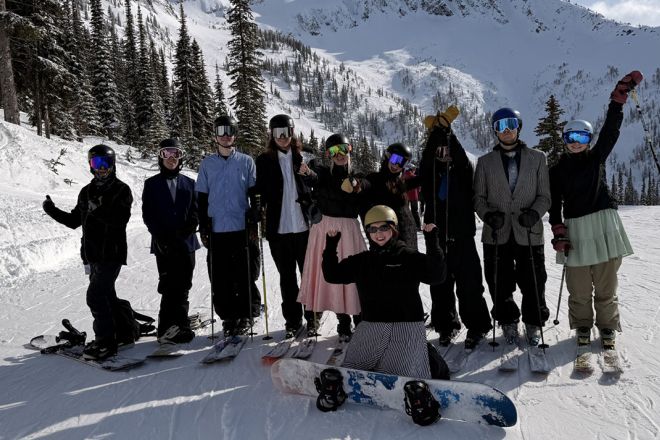 Skiers and snowboarders stand on the mountain in black-tie attire
