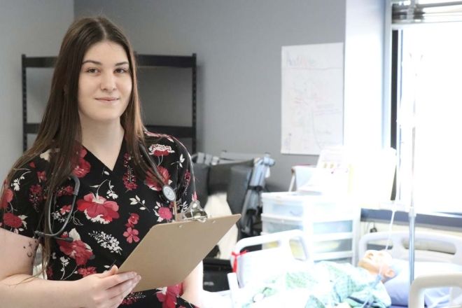 A Practical Nursing student stands in the lab holding a clipboard