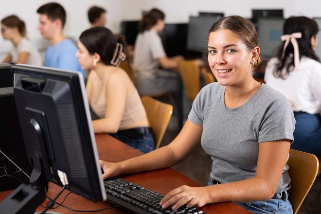 A student sits at a computer smiling