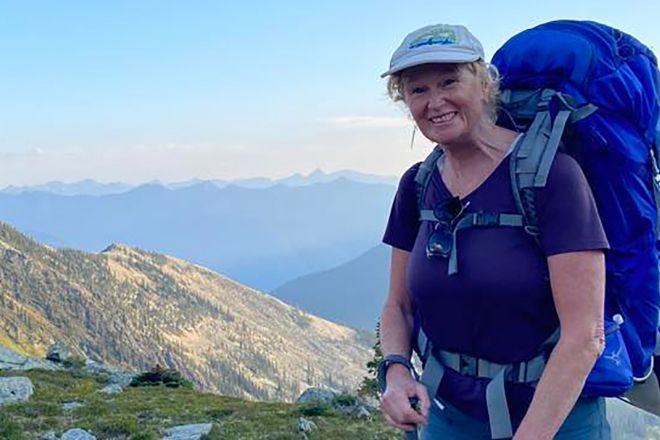Allison Alder stands in the alps wearing a hiking backpack