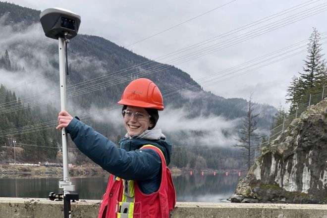 A person wearing a hard hat and high vis vests holds a piece of equipment