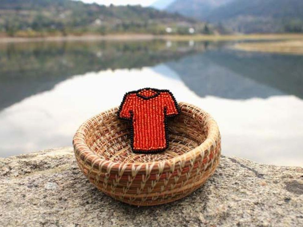 A beaded orange shirt in a basked next to a lake